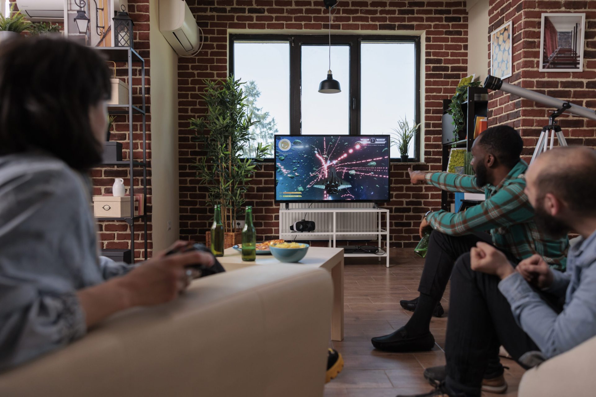 Diverse friends using tv console and joystick to play video games, having fun at house gathering with beer bottles. Group of people enjoying shooting competition with gaming strategy.